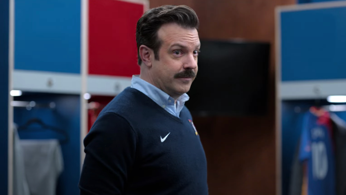 Jason Sudeikis stands in the middle of the room and stares in Ted Lasso.