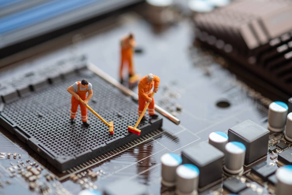Small models of workmen cleaning up a computer motherboard with brushes